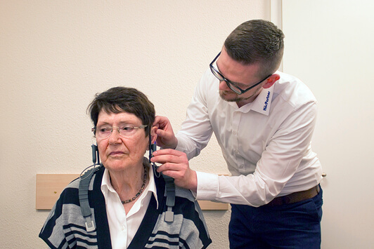 Ein Hörakustiker passt einer Seniorin ein Hörgerät im Hörstudio an.