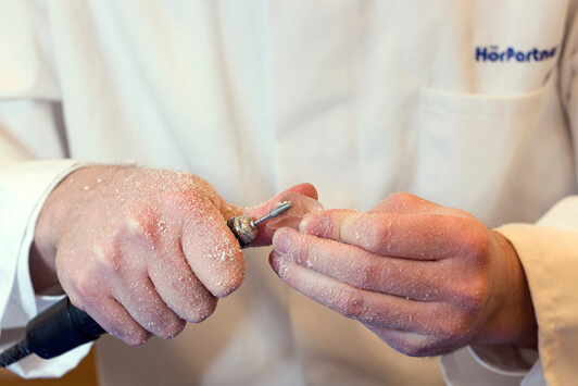 Ein Hörakustiker schleift ein Hörgerät präzise mit einer elektrischen Feile.